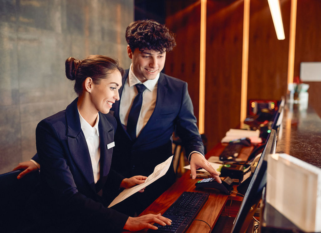 To hotelreceptionister samarbejder ved computeren, der repræsenterer teamwork, effektiv vagtplanlægning og arbejdsstyring